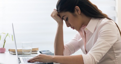 a stressed woman on her laptop, with her head resting on her hand