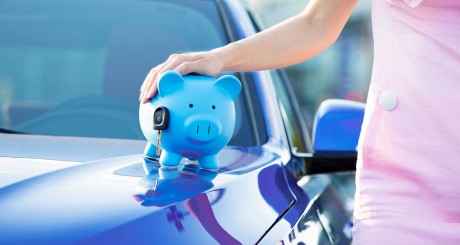 a woman touching a piggy bank that is resting on the hood of a car