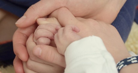 four adult hands cradling an infant's hand