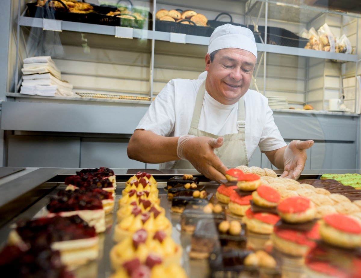 a caterer wearing a hat prepares a variety of pastries for an upcoming event